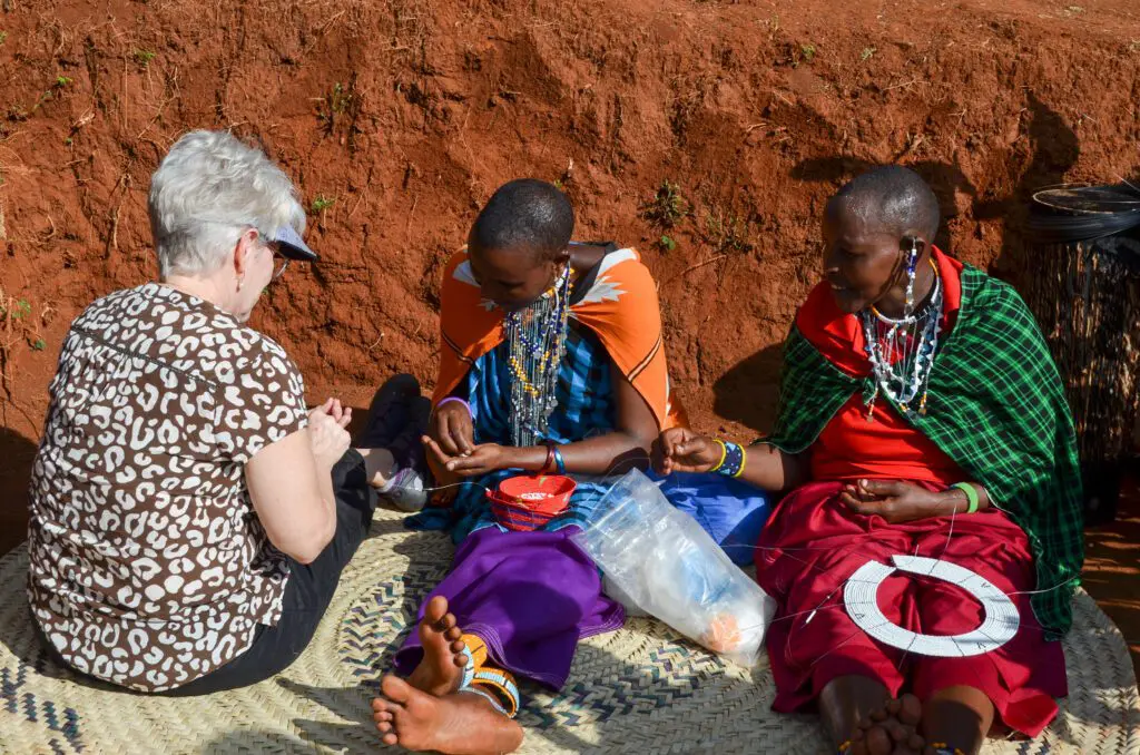 two maasai girls teaching beadwork to a tourist visiting the maasai ecolodge.